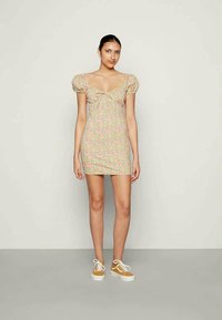 Vestido mini floral com mangas bufantes em cores suaves; design ajustado com um decote em V e detalhe em laço, combinado com ténis bege.