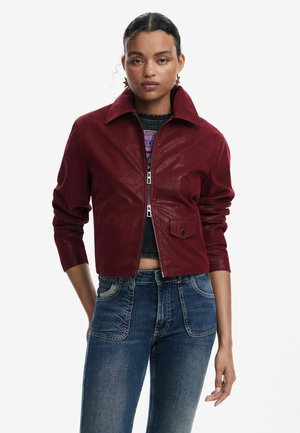 Rote Leder-Cropped-Jacke mit klassischem Kragen, Reißverschluss und einer Vordertasche; kombiniert mit blauen Jeans.
