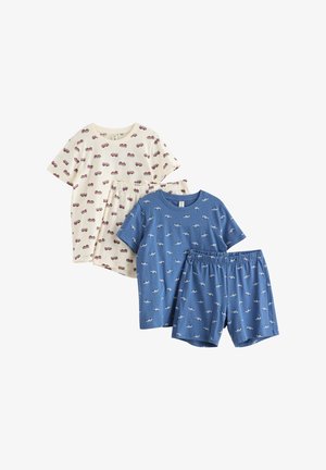 Jeune garçon debout pieds nus, portant une chemise bleue à manches courtes et un short avec de petits motifs de voitures blanches sur un fond blanc uni.