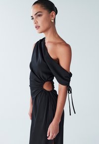 Juoda satino suknelė su asimetrišku iškirpimu, raukšlėta detale, šoniniu išpjovu ir reguliuojamomis surištomis rankovėmis. Lygi tekstūra.