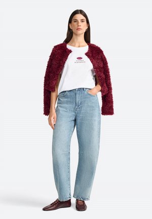 Veste en fausse fourrure bordeaux sur un T-shirt blanc avec le motif "CHERRY ELEGANCE", associée à un jean large bleu clair et des chaussures bordeaux foncé.