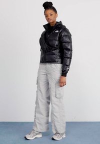 Črn napihnjen plašč z kapuco, zadrgo in stranskimi žepi; v kombinaciji z svetlo sivo vojaškimi hlačami in lahkimi supergami.