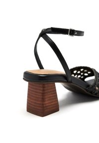 Sandale en cuir noir avec un design tissé, dotée d'un talon en bois et d'une bride de cheville ajustable pour un maintien sécurisé.