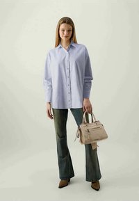 Camisa azul clara com riscas, de corte descontraído; combinada com jeans verdes desbotados e uma bolsa bege. Sapatos castanhos pontiagudos completam o visual.