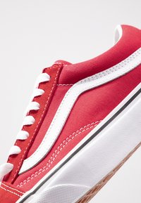 Rød kanvas sneaker med et hvitt bølgedesign, som har hvite snorer, en hvit mellomsåle og en teksturert gummisåle med brune detaljer.