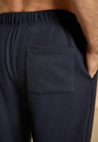 Sötétkék, textúrált joggerek, illeszkedő, rugalmas derékpánttal és négyzet alakú hátsó zsebével, váffel kötésű anyagból készült.