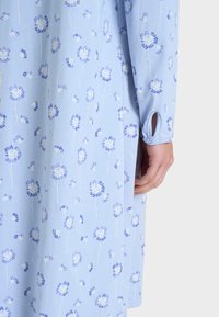 Abito azzurro chiaro realizzato in tessuto morbido, caratterizzato da un motivo floreale in blu scuro. Ha un dettaglio con polsino abbottonato sulla manica.