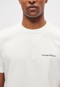 Biele bavlnené tričko s klasickým strihom, vybavené rebrovaným okrúhlym golierom a malým čiernym vyšívaným logom na ľavej strane hrudníka.