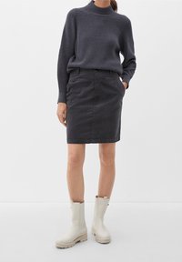 Jupe en velours côtelé gris foncé, slim-fit, avec poches avant, associée à un pull texturé sombre et des bottes en caoutchouc crème montantes jusqu'aux genoux.