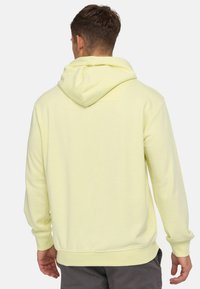 Sudadera con capucha de color amarillo claro, de manga larga, con puños y dobladillo acanalados. Textura suave; el bolsillo canguro no es visible desde atrás.
