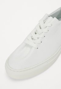Baskets blanches en cuir texturé avec des lacets plats, bout rond et semelle en caoutchouc présentant un motif de traction subtil.