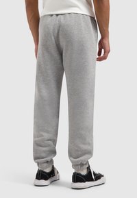 Grijze sweatpants van zachte stof, met elastische manchetten en een tailleband met trekkoord, gecombineerd met zwarte sneakers en witte veters.