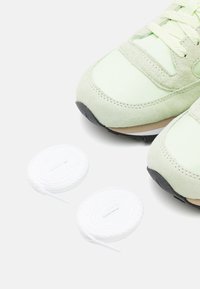 Atletske cipele u mint zelenoj boji imaju kombinaciju glatkog sintetičkog materijala i antilopa, s crnim gumiranim potplatima i bijelim okruglim vezicama pored njih.