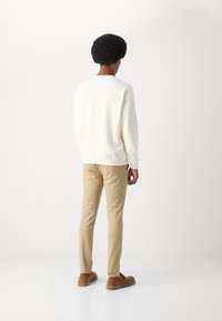 Hvid sweatshirt med en afslappet pasform, beige slim-fit bukser og brune ruskindsko. Glat tekstur, minimalistisk design, ingen synlige mønstre.
