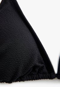 Close-up van een zwart, textuurgegeven bikini-top met geplooide onderband en verstelbare bandjes.