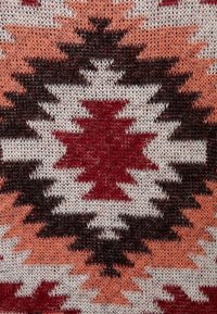Tkactwo z wzorem w odcieniach czerwieni, brązu, bieli i brzoskwini. Wzór zawiera kształty geometryczne oraz motywy zygzakowate. Miękka, teksturowana tkanina.