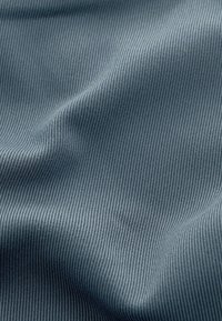 Textil med en slät, texturerad yta i en dämpad blågrå färg som har fina, jämna vertikala ränder genom hela mönstret.