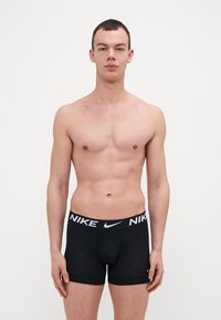 Svart boxertruser for menn med en myk elastisk midje med en hvit Nike-logo. Stoffet er glatt med et subtilt logomønster.