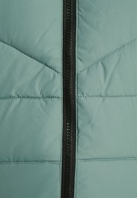 Light green puffer jacket featuring a black zipper down the center, with stitched quilted texture and geometric panel design.