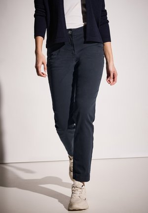 Tmavě modré bavlněné kalhoty slim fit s knoflíkovým zapínáním a bočními kapsami, spárované s světle barevnými teniskami.