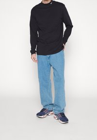 Černé tričko s dlouhým rukávem, světle modré volné džíny a tmavě modré tenisky s růžovými detaily. Tričko má na hrudi malé logo.