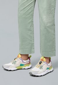 Weißer Sneaker mit mehrfarbigen Akzenten in Grün, Gelb und Lila. Verfügt über strukturierte Overlays, einen gepolsterten Schaft und eine Gummisohle.