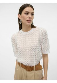 Top de punto blanco con un patrón texturizado, mangas cortas abullonadas y un escote redondo, combinado con pantalones beige claros y un cinturón marrón.