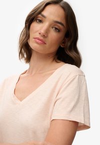 Lyserød V-hals t-shirt med korte ærmer, lavet af blødt stof; har en afslappet pasform og subtile teksturer over det hele.