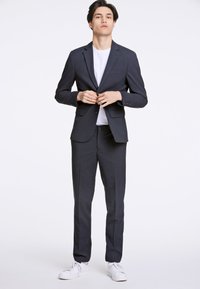 Marineblauw pak met een op maat gemaakte blazer met gekerfde revers, een enkele knoopsluiting en bijpassende broek. Draag dit over een wit T-shirt, gecombineerd met witte sneakers.