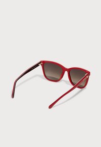 Red cat-eye sunglasses with a glossy finish, dark tinted lenses, and black patterned interior accents on the arms. Gold hardware details.