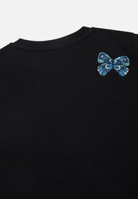 Zwarte katoenen t-shirt met een getextureerde blauwe en teal mozaïekpatroon strik appliqué aan de bovenkant aan de linkerkant.