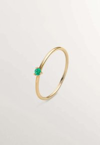 Anillo de oro con una banda delgada. Presenta una piedra preciosa verde redonda engastada en un diseño de garras en la parte frontal. Acabado suave y pulido.