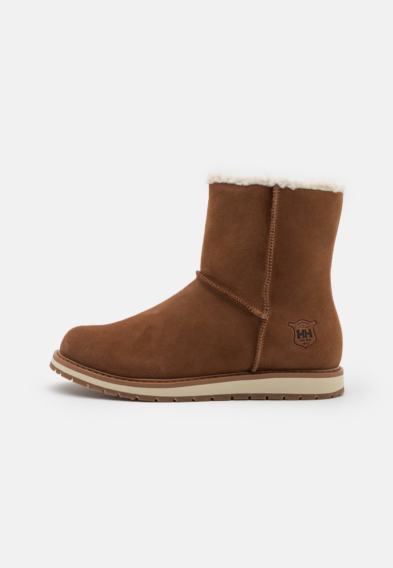Botas de ante marrón hasta el tobillo con un forro de borrego blanco, suela plana beige y detalle de logo en el exterior. Diseño simple con costuras mínimas.