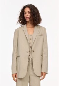 Beige pinstriped blazer with notch lapels, single button closure, and flap pockets, paired with a matching top featuring buttons.