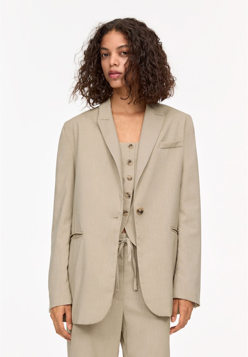 Beige pinstriped blazer with notch lapels, single button closure, and flap pockets, paired with a matching top featuring buttons.