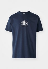 Mørkeblå bomulls t-skjorte med korte ermer, rund hals og et hvitt grafikk som viser et våpenskjold og teksten "the new originals".