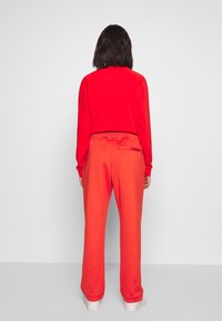 Rode sweatshirt met een ontwerp op de achterkant, gecombineerd met oranje taps toelopende joggers met een elastische tailleband en zijzak, gladde stoftextuur.