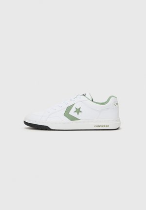 White low-top sneakers made of synthetic material with green accents, featuring a star logo, flat laces, and a black rubber sole.