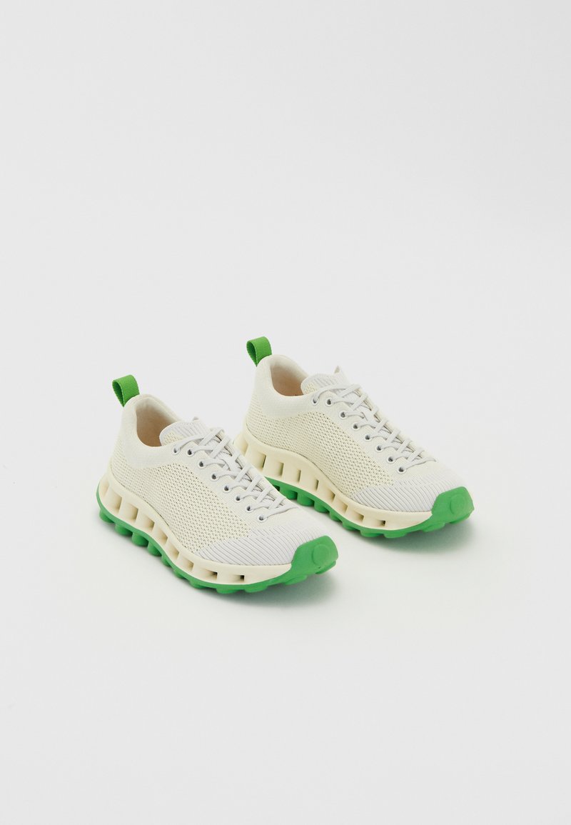 Baltas siets sneakers ar zaļām gumijas zālēm un akcentiem, ar apaļu purngalu un mīkstinātu vidusdaļu ar izgriezumiem.