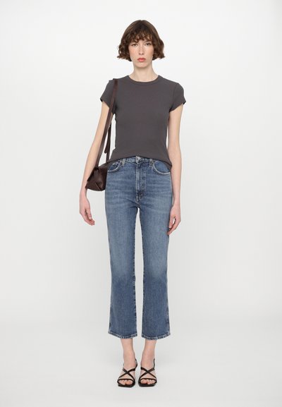Grå tajt t-shirt, högmidjade ljusblå jeans med utsvängd nederkant, svarta sandaletter med remmar och en liten brun handväska.