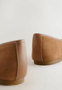 Brune ruskind slip-on sko med glatte læderdetaljer, der har et lavprofil-design og en fleksibel gummisål.