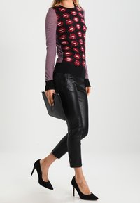 Gestrickter Pullover mit rotem Lippenmotiv auf schwarzem Hintergrund, gestreiften Ärmeln, kombiniert mit schwarzer Lederhose und schwarzen spitzen High Heels.
