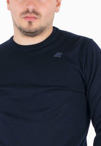 Modra dolga rokavičasta majica iz tkanine, z okroglim izrezom in majhnim črnim logotipom na prsih. Mehak material in oprijet kroj.