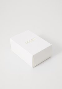 Hvit rektangulær boks med teksturert overflate, med en gull "GUESS" logo på toppen. Enkelt design, rene kanter og ingen synlig maskinvare.