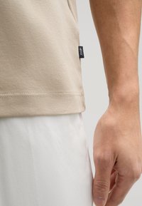 Beige katoenen t-shirt met korte mouwen, zijnaadlabel en een gladde structuur. Gepaard met witte broeken, die een ontspannen pasvorm laten zien.