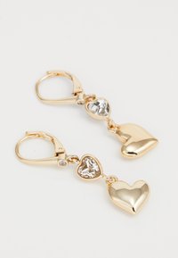 Boucles d'oreilles en forme de cœur doré, mettant en vedette un cœur en cristal transparent et un charme cœur lisse, tous deux suspendus à des fermoirs à ressort.