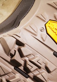 Podeszwa gumowa z misternymi wzorami bieżnika dla lepszej przyczepności, teksturowanym brązowym wykończeniem oraz wyraźnym żółtym logo Vibram.