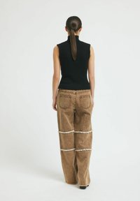 Fekete, bordás, ujjatlan top, amelyet magas derékú, barna, széles lábú nadrággal párosítottak, frufrus vízszintes varratokkal és hátsó zsebekkel.