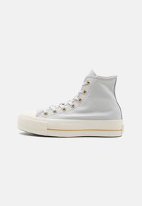 Deportivas altas de lona gris claro con ojales dorados, puntera de goma blanca y suela blanca con una franja dorada.