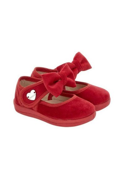 Scarpe Mary Jane in velluto rosso con un grande fiocco sopra, punte arrotondate e un accento metallico a forma di cuore sul lato. Texture morbida, suola piatta.